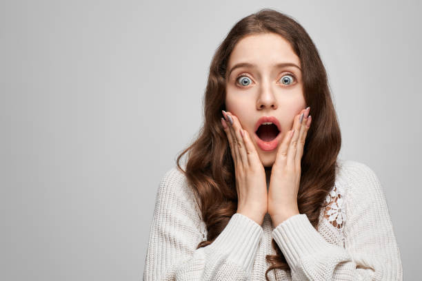 Fille choquée avec la bouche ouverte, les mains sur les joues et des gros yeux